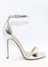 Ali Heels in Silver as the feet is propped on a marble table is the back ground. It is pictured on a side view as you see buckle around the ankle. Ali Heels in Silver is a heel that is covered in the back of the heel and has a thick to thin to thick strap in the front showing your toes.