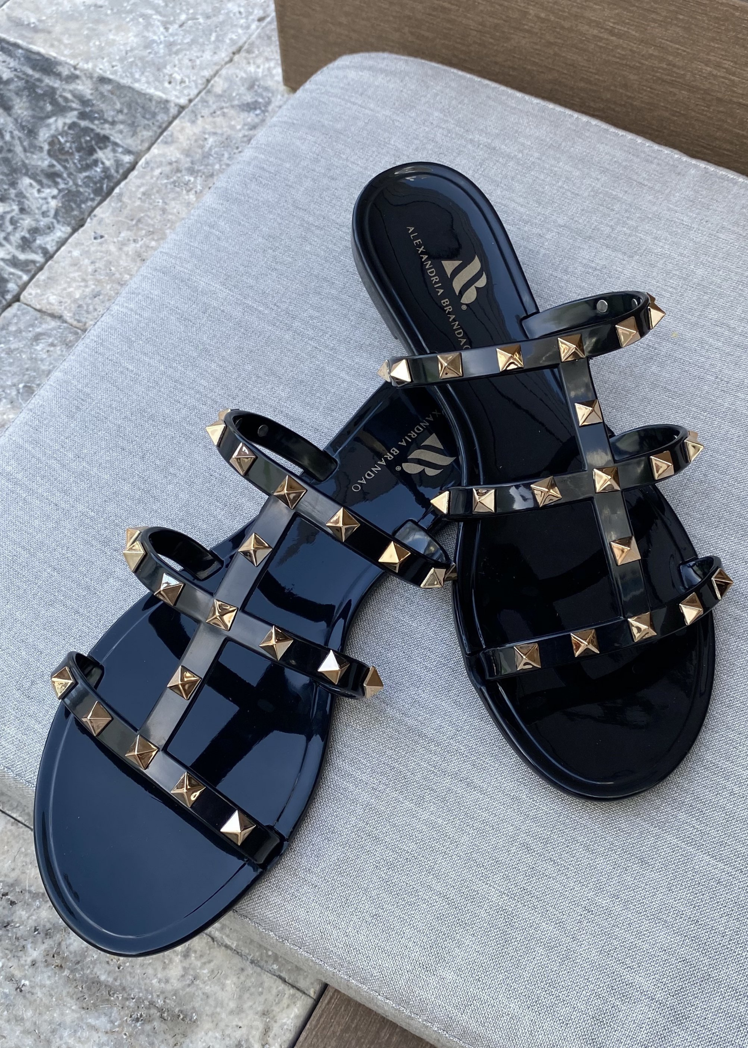 Aurora Black Jelly sandal that has  Gold Studs on all straps and is a slip on sandal.  Sandal has three equally separated horizontal straps that goes all the way to top of the bridge of the foot and one strap in the middle connecting all straps