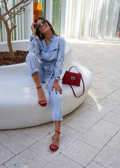 @carlanunez_ styled in a jean jumpsuit and accessorized with our Aria scarlet jelly sandals.