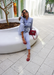 @carlanunez_ sitting with one leg up dressed in a jean jumpsuit and accessorized with Aria red jelly sandals and red purse