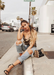 @jamialix sitting on a curve in Beverly Hills, California  wearing Ali heels in Black with ripped light acid washed jeans  and a gold top.