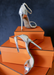 Silver Metallic "Ali" sandal heels propped up on orange boxes.