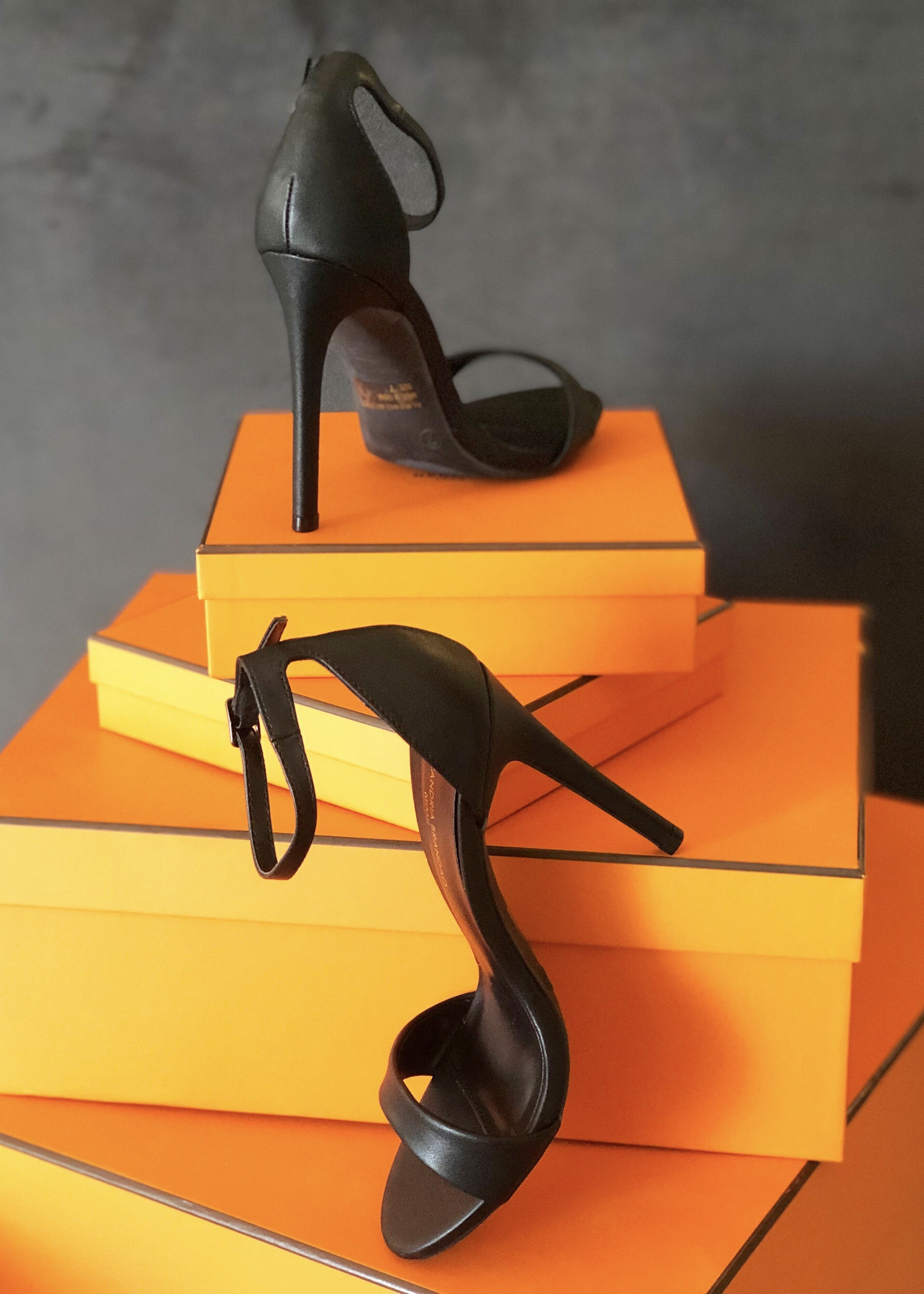 Our Black Ali sandal heels propped up on orange boxes.