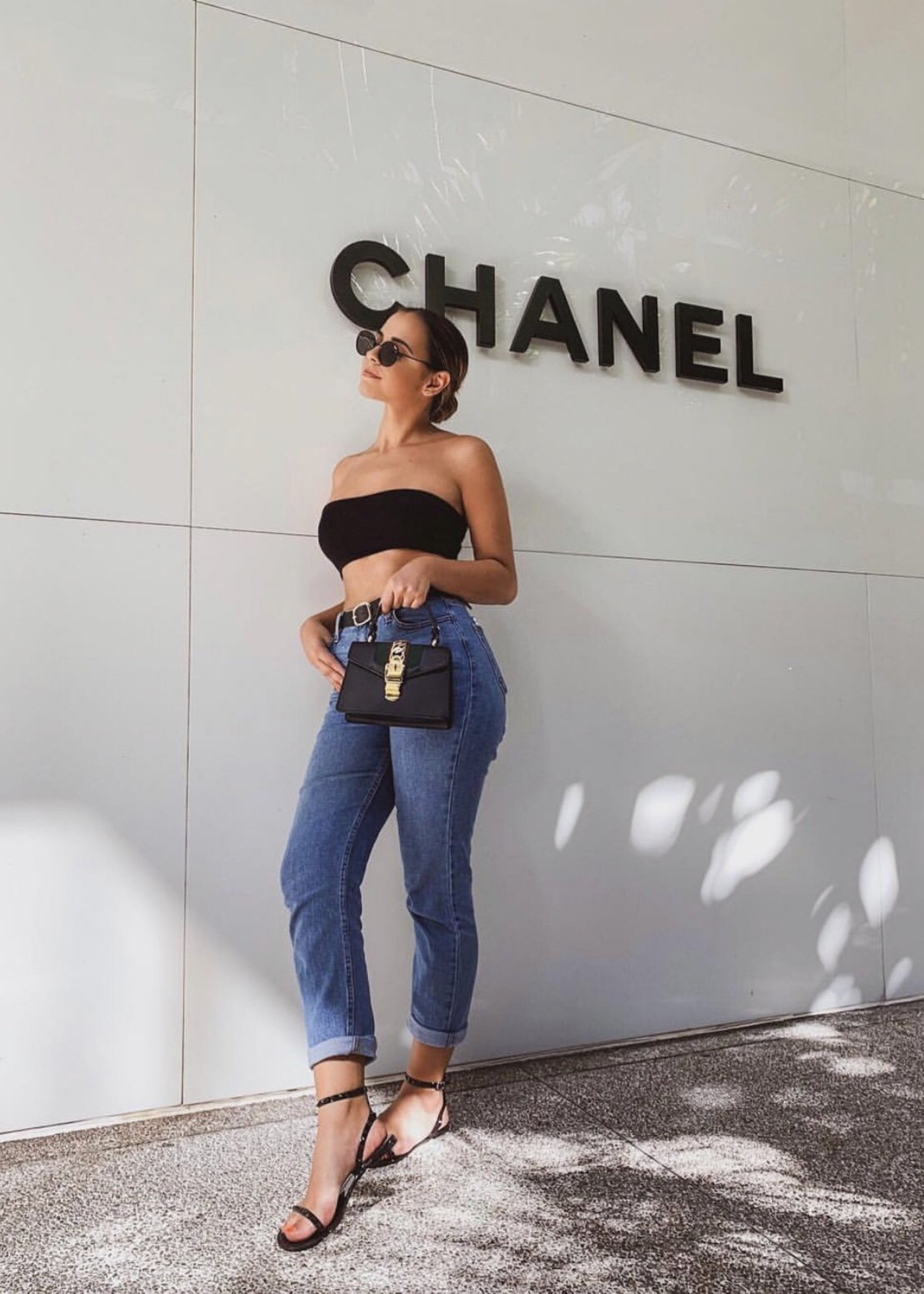 @gabiiiking via Instagram wearing Aria sandals in Black standing by the Chanel store.