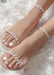 Womens feet propped up on a white fur rug wearing Nude Aris sandals.